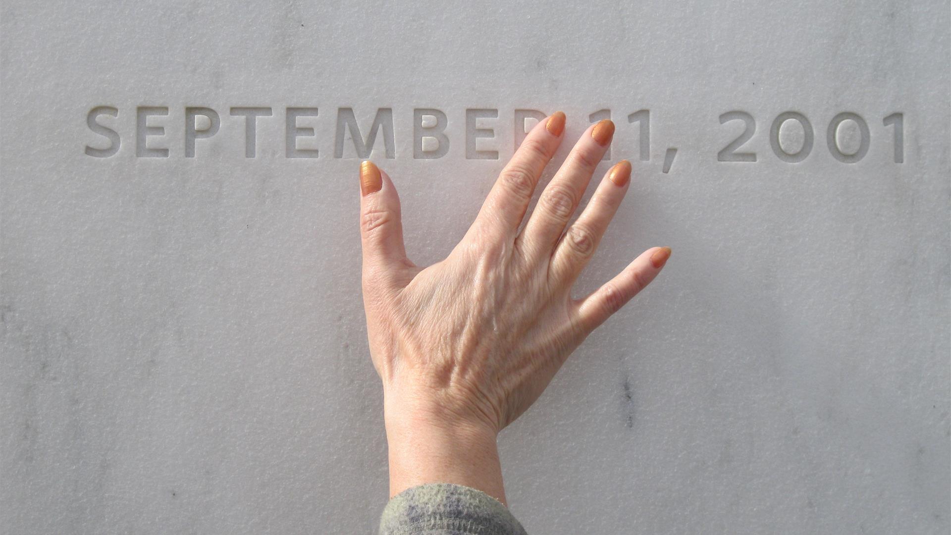 a hand placed over the September 11 date engraved on a wall
