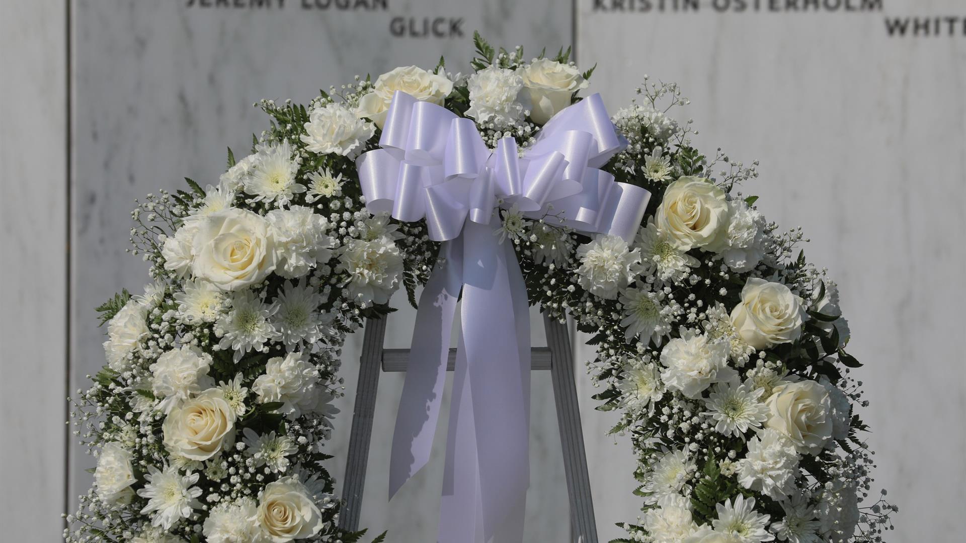 A wreath with cream colored flowers and a big white bow.