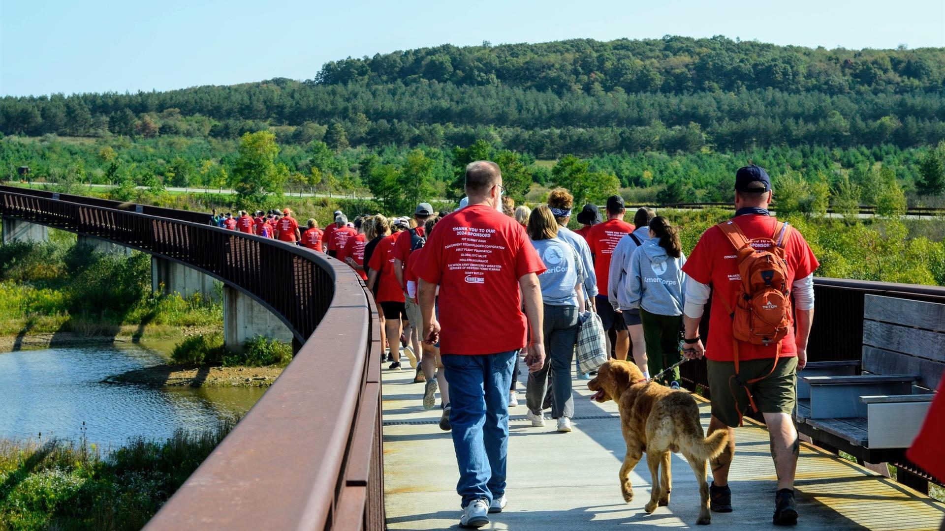 People walking on a bridge over a large pond.